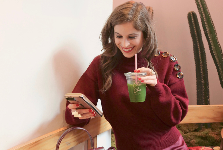 white woman with brown hair sipping a matcha wearing a red sweater