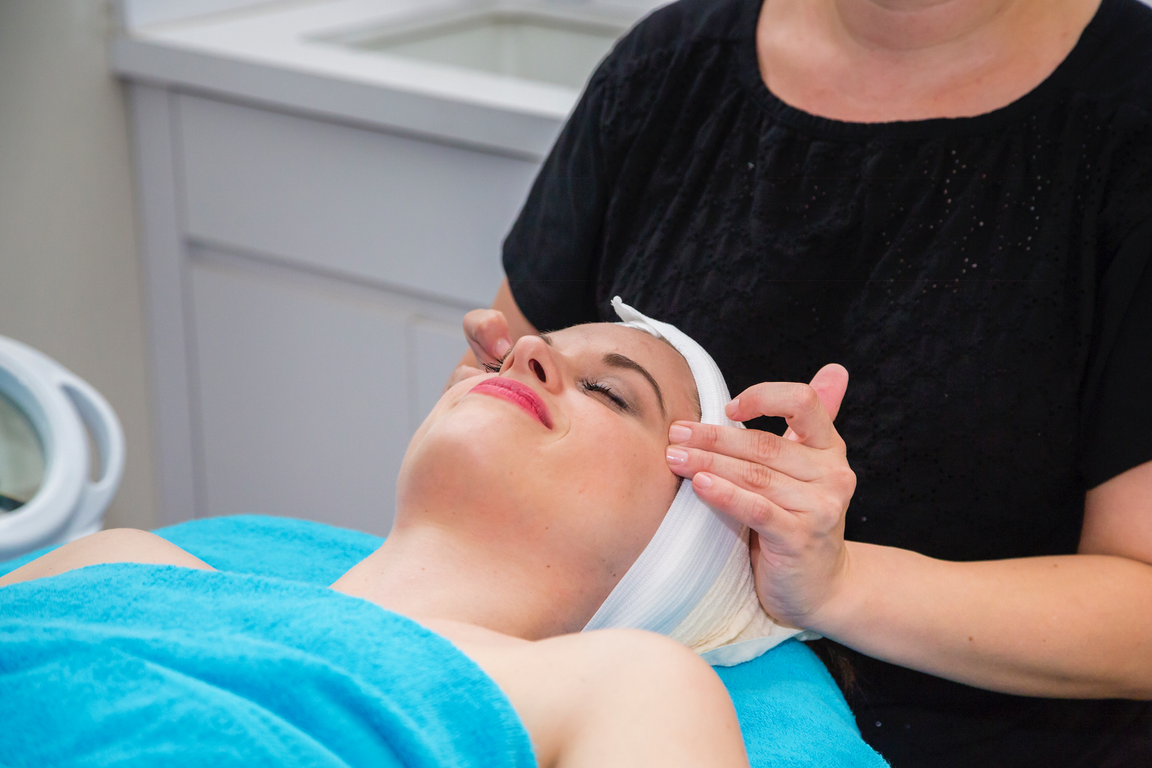 Woman laying down getting a facial: she has on pink lipstick and is covered by a blue blanket