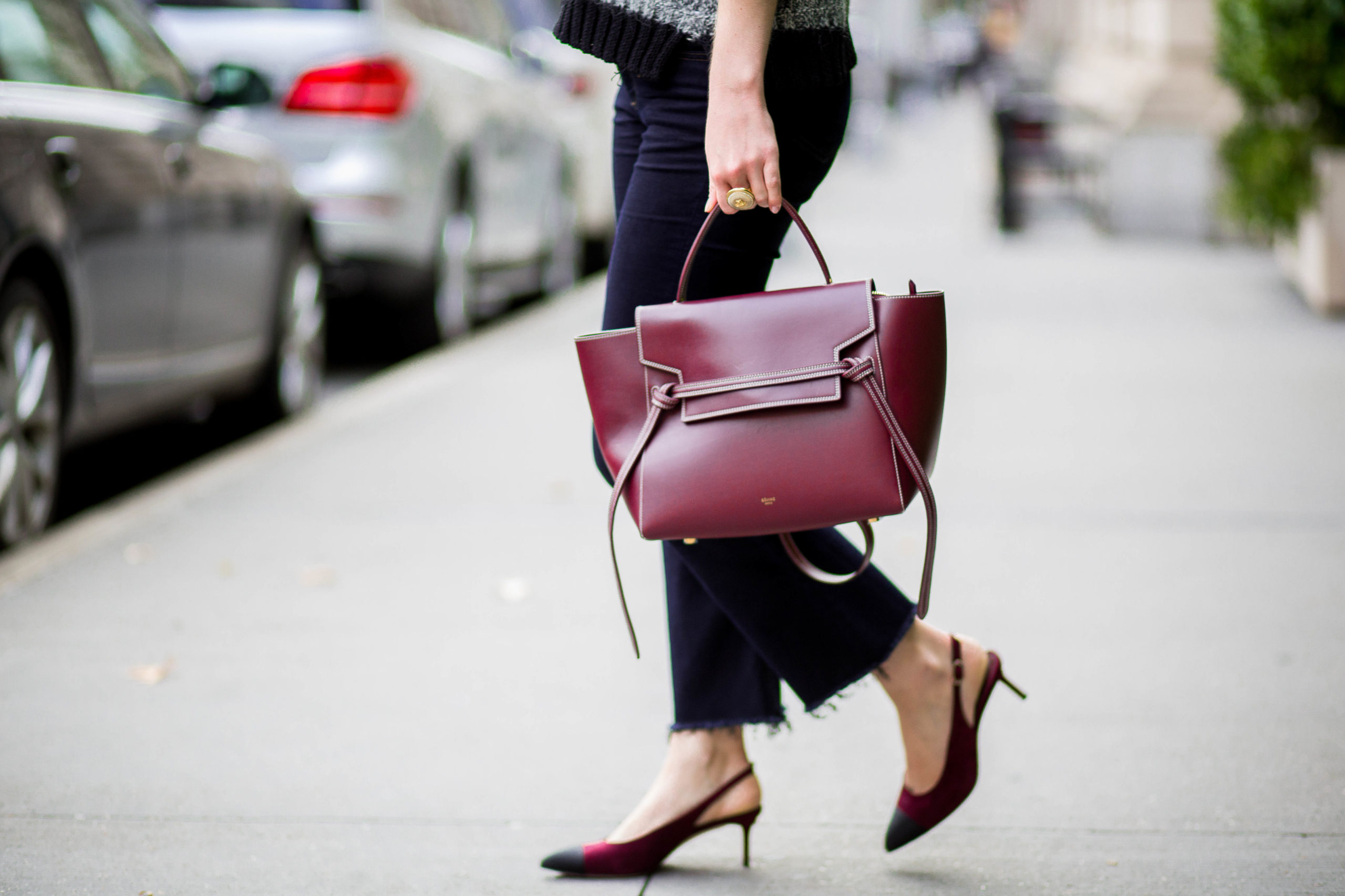 Woman walking across the sidewalk in Manhattan wearing jeans, carrying a crimson purse, wearing jeans and kitten heels