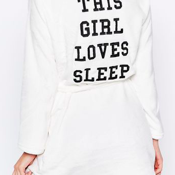 Picture of a girl turned around wearing a white robe that says: this girl loves sleep