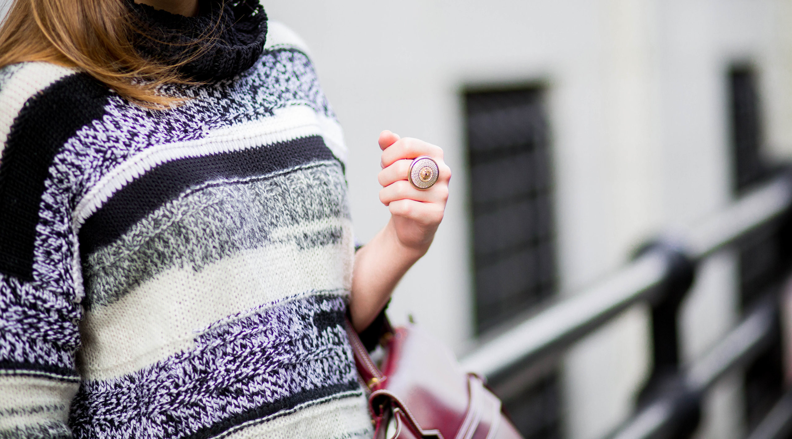 Close up of a woman wearing a black & white sweater, a gold ring & a crimson bag