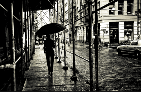 Person walking down the street in the rain holding an umbrella: black and white photo