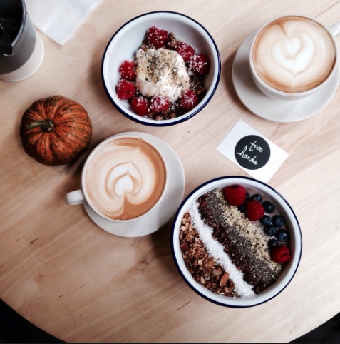 Brunch spread at Two Hands NYC: two lattes with heart latte art, an açaí bowl and some oatmeal on a wooden table with a pumpkin on the table