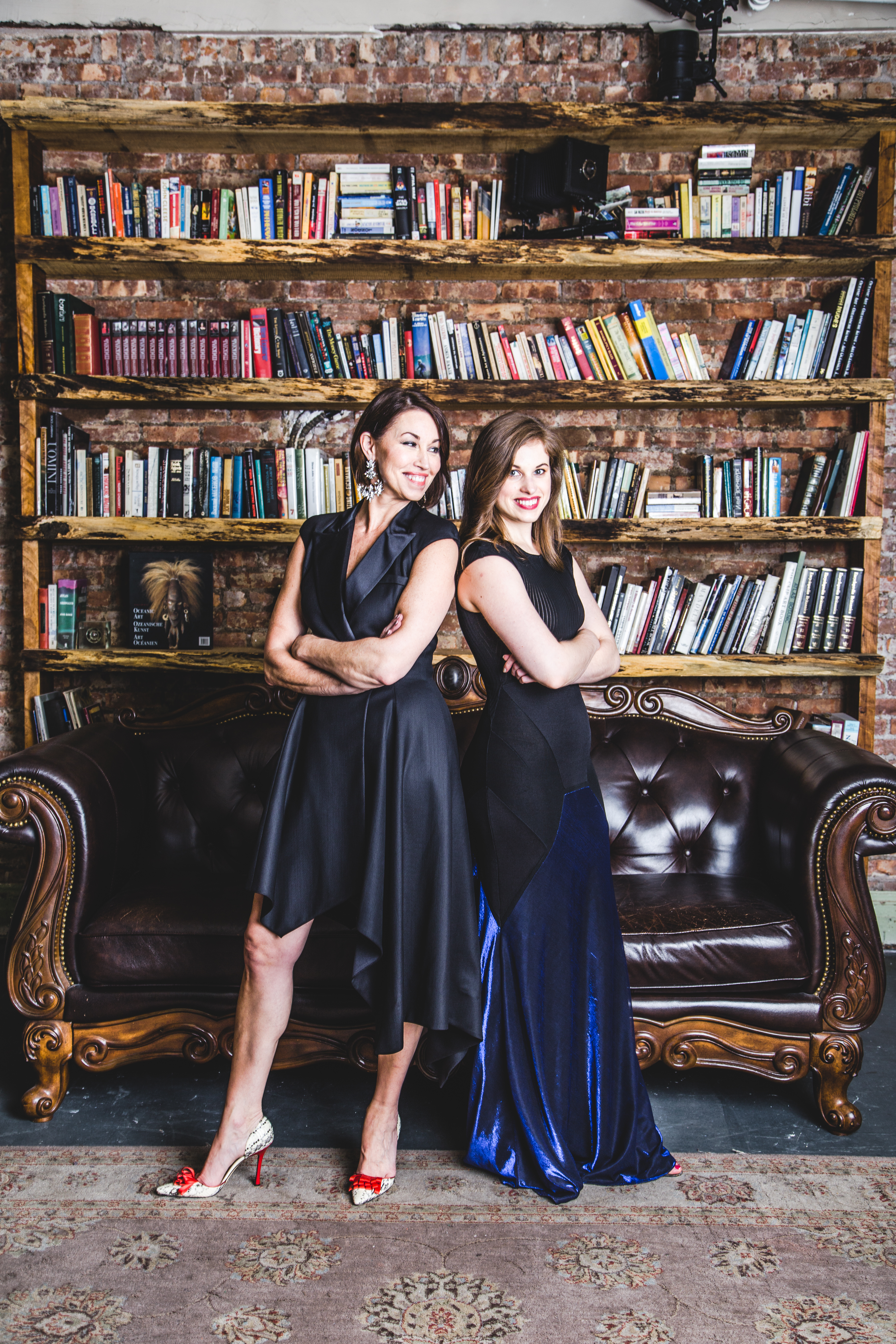 two women standing in a library wearing black cocktail dress, both have brown hair