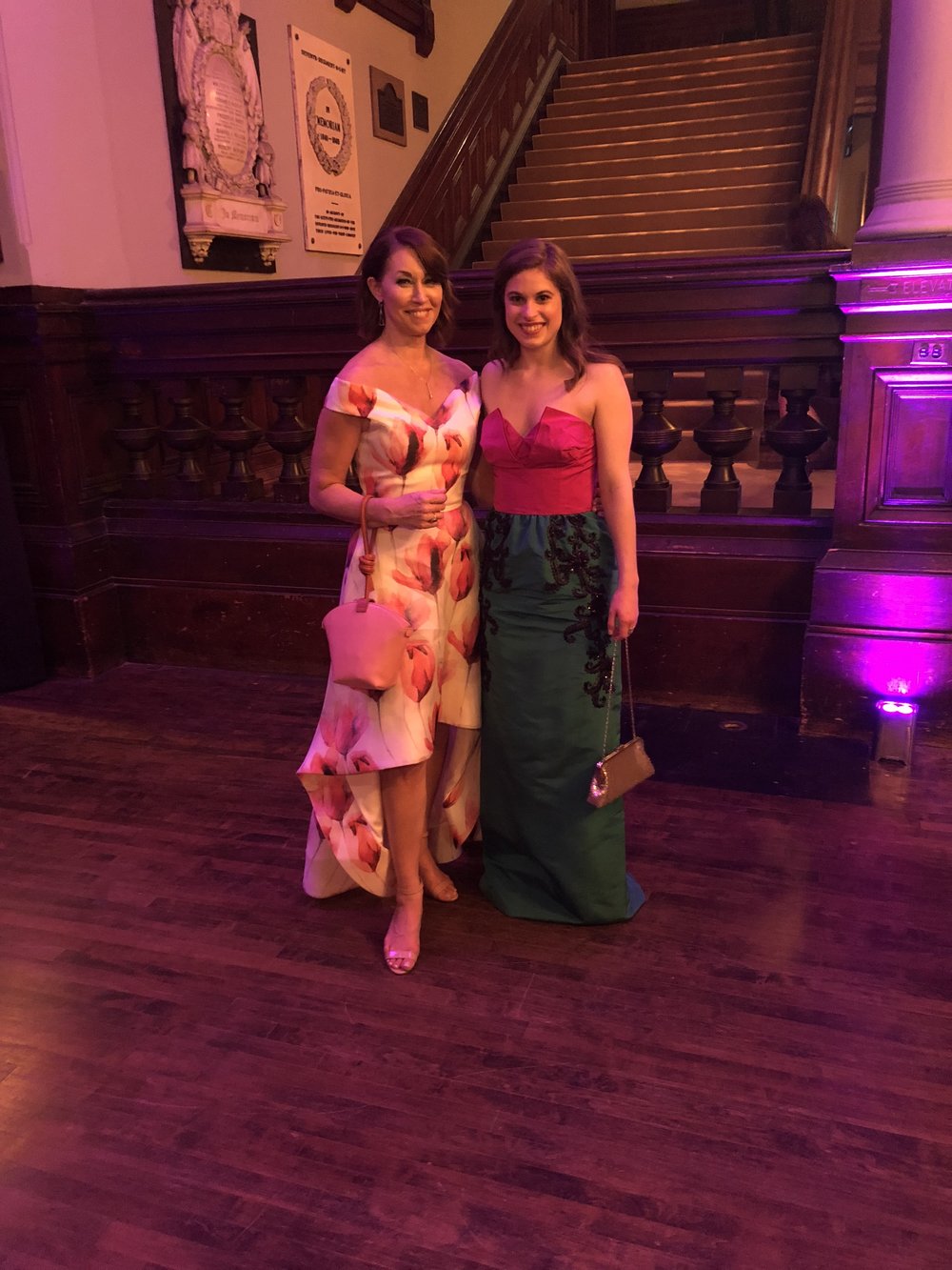 Two women at the Park Avenue Armory: one wearing a floral high low gown and the other wearing a pink and green gown