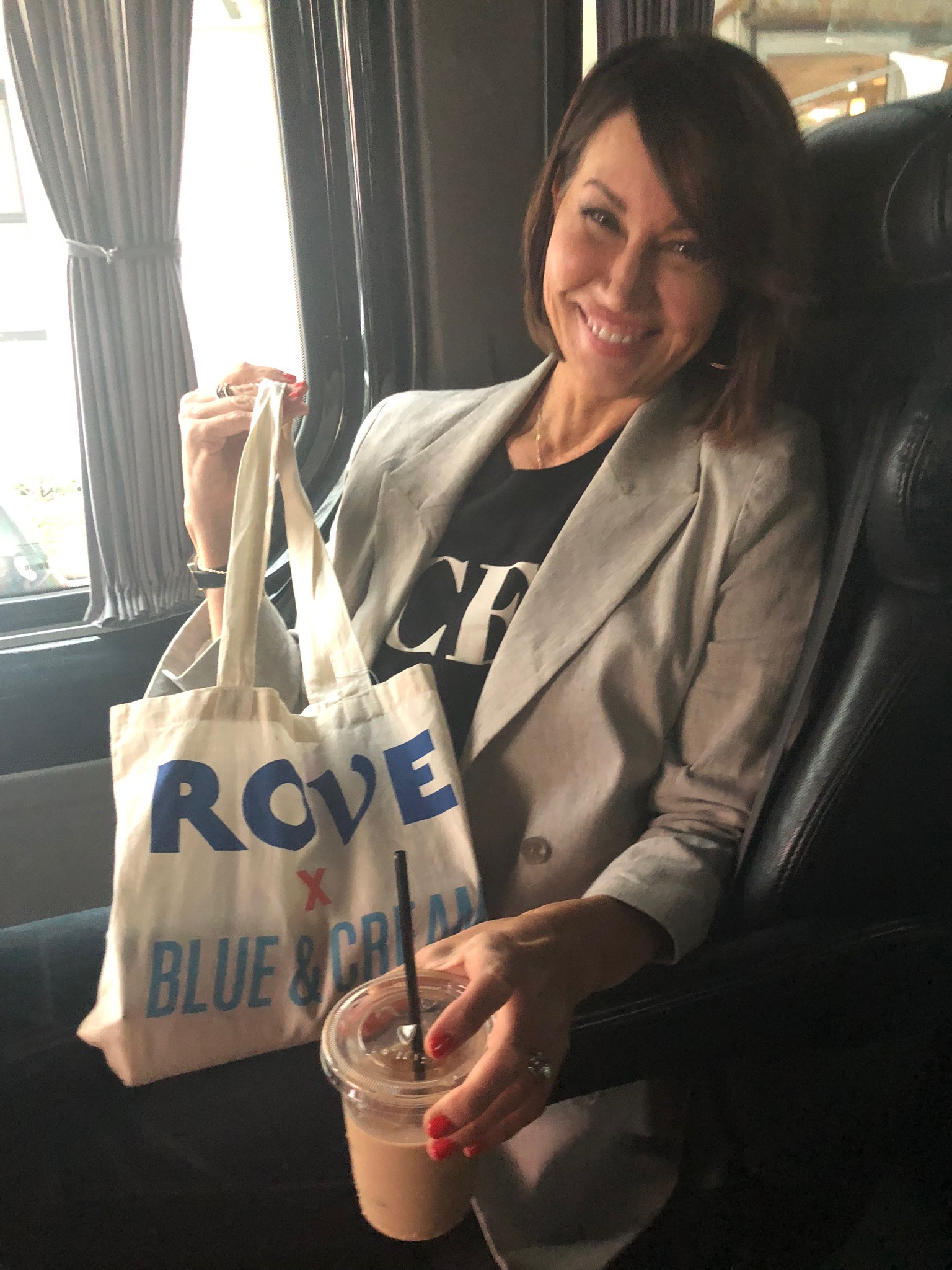 Women sitting in a bus holding up a goodie bag and holding an iced coffee