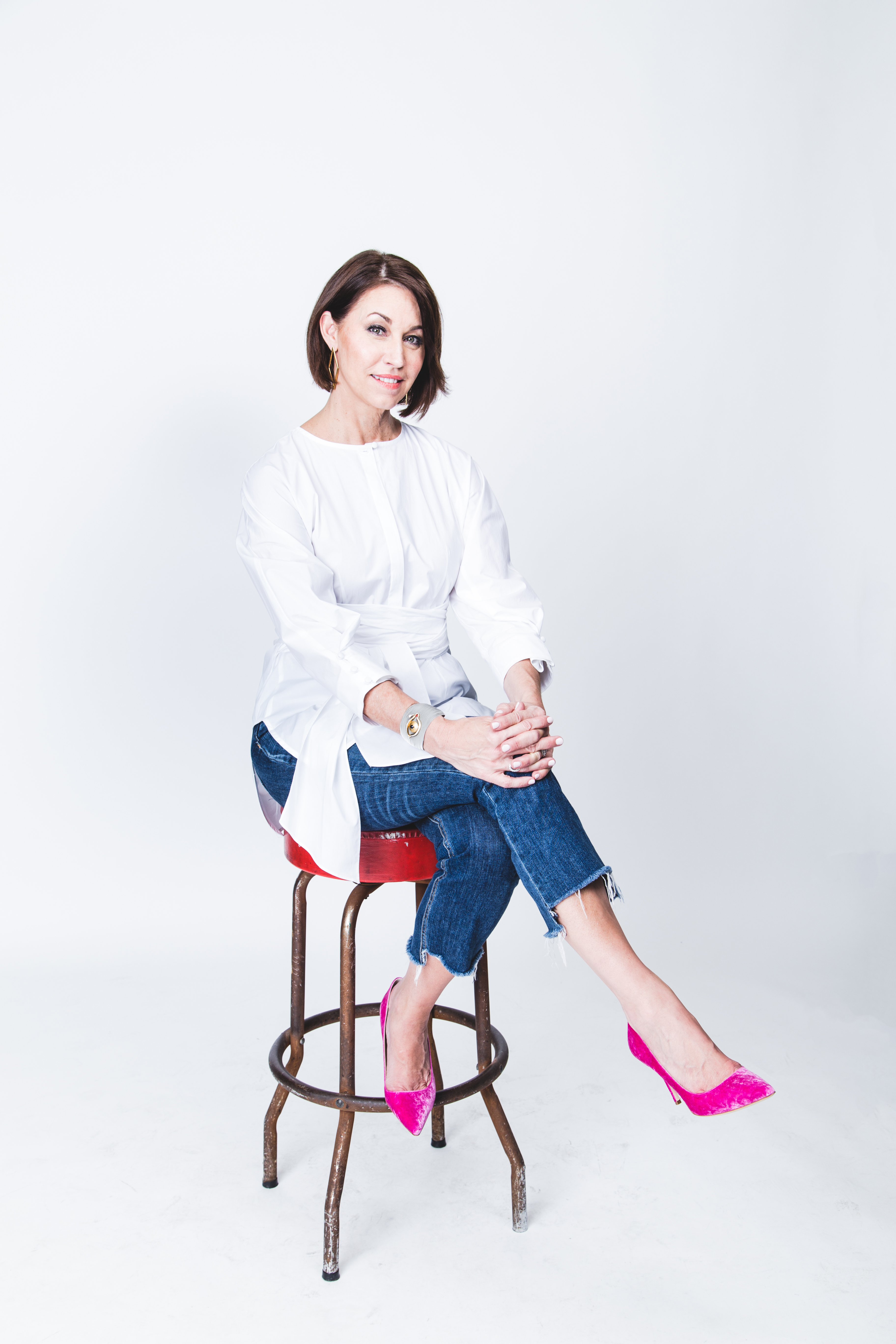Woman wearing a white cotton top, jeans and pink shoes sitting on a stool
