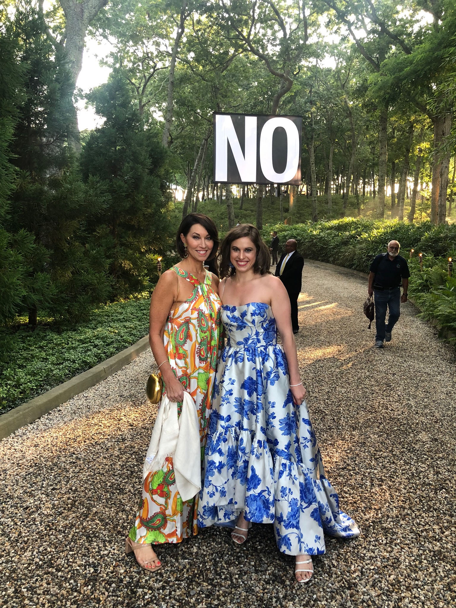 Two women standing in a forest wearing black tie both in printed long dresses