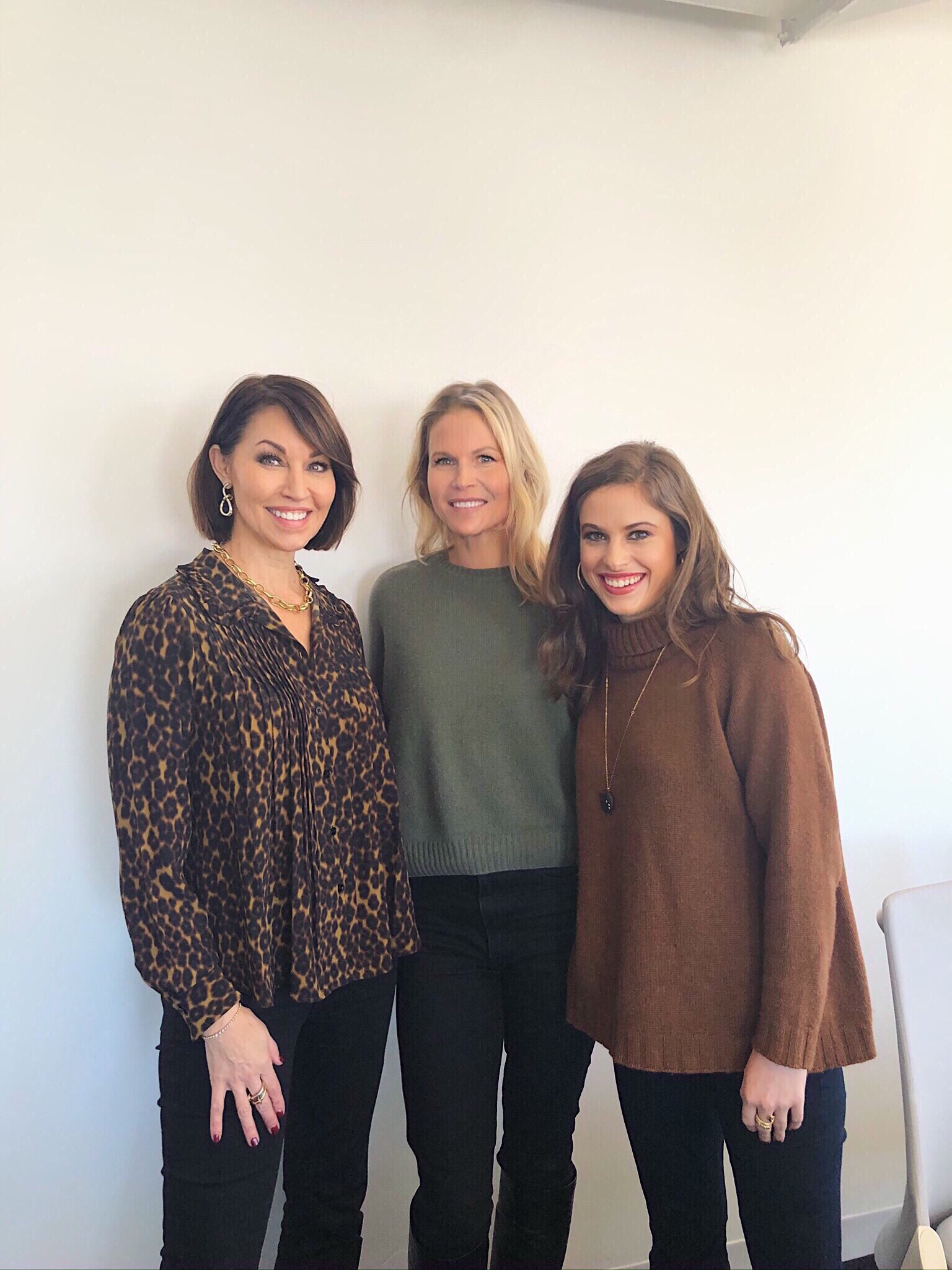 Three women: one wearing a long-sleeve leopard print top, one in a green sweater with blonde hair the last in a camel colored turtleneck sweater. The other two have brown hair