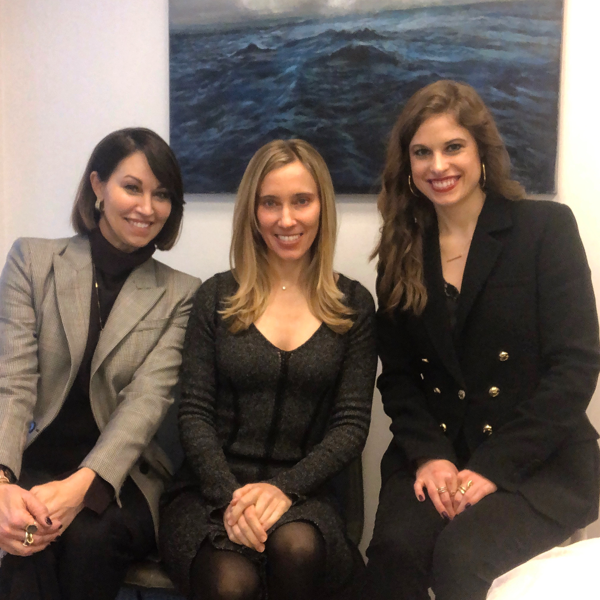 Three women: one wearing a plaid blazer & black turtleneck with brown hair, one blonde wearing a grey dress and one curly brunette wearing a black blazer