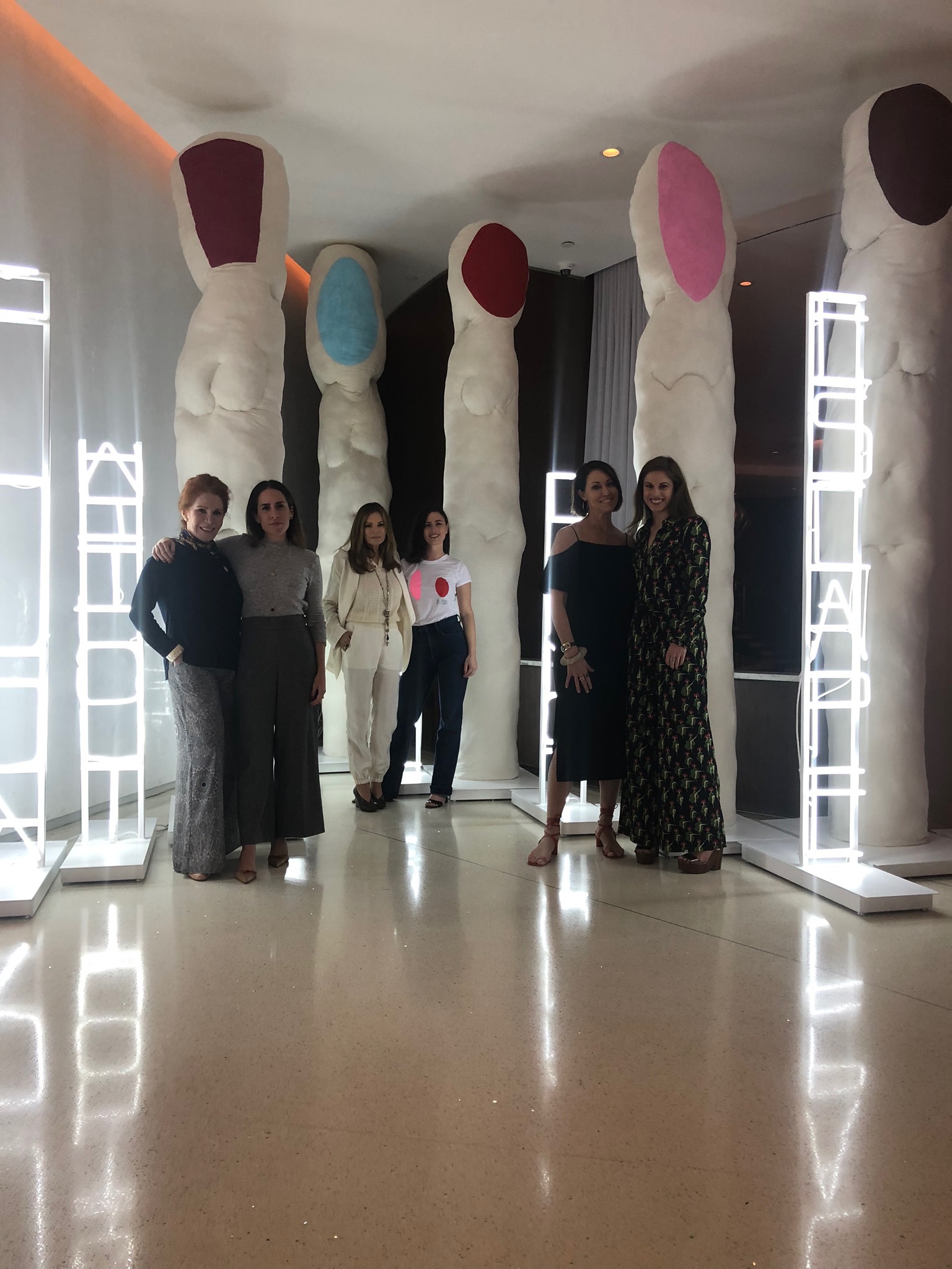 six women in pairs standing in front of an art sculpture