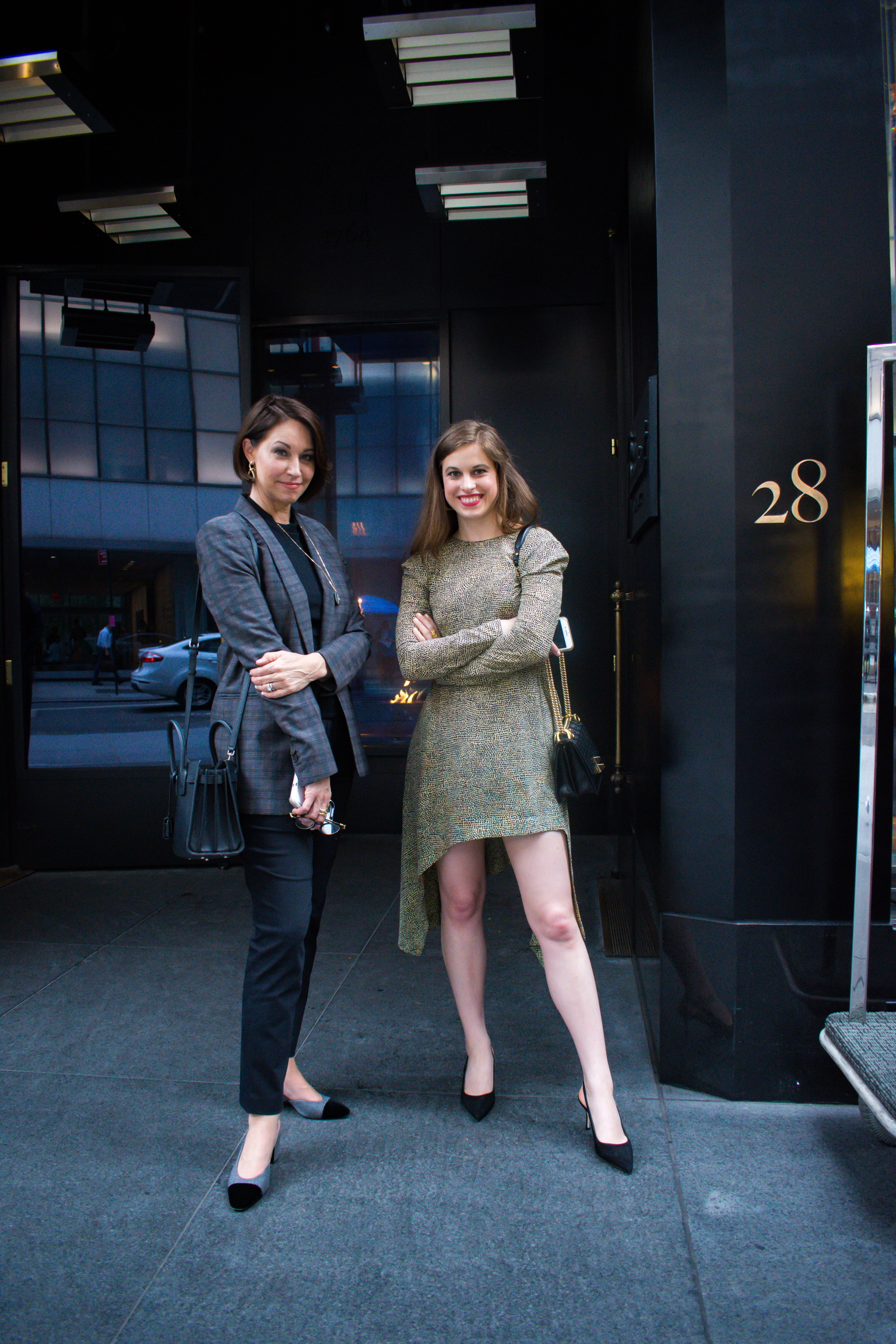 Two women both with brown hair: one with a plaid blazer and black skinny pants with slingback pumps and the other wearing a printed mini dress with black slingback pumps