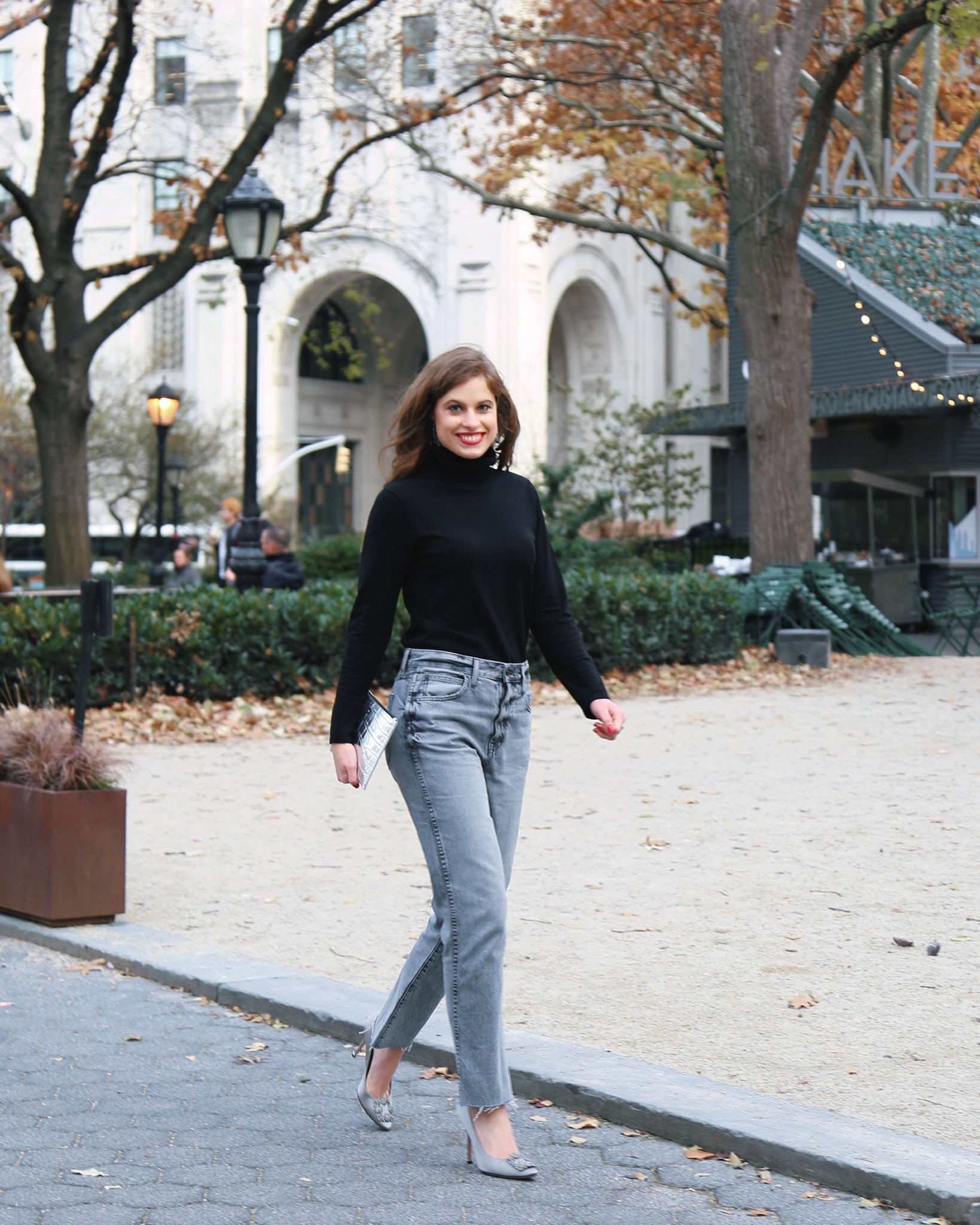 Woman walking in Madison Square Park in Manhattan wearing a black turtleneck tucked into grey SLVRLAKE jeans wearing grey Manolo Blank heels. Curly hair