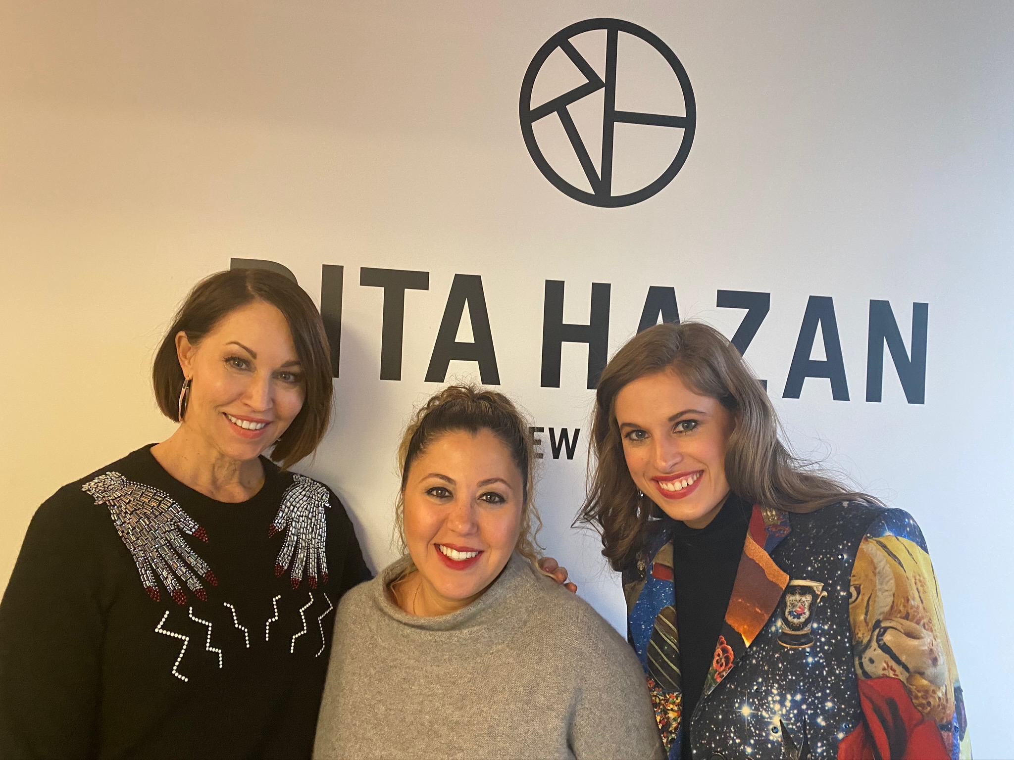 Three women: one in a black sweater with crystal hands, a woman in a grey sweater (Rita Hazan) and a woman in a colorful blazer