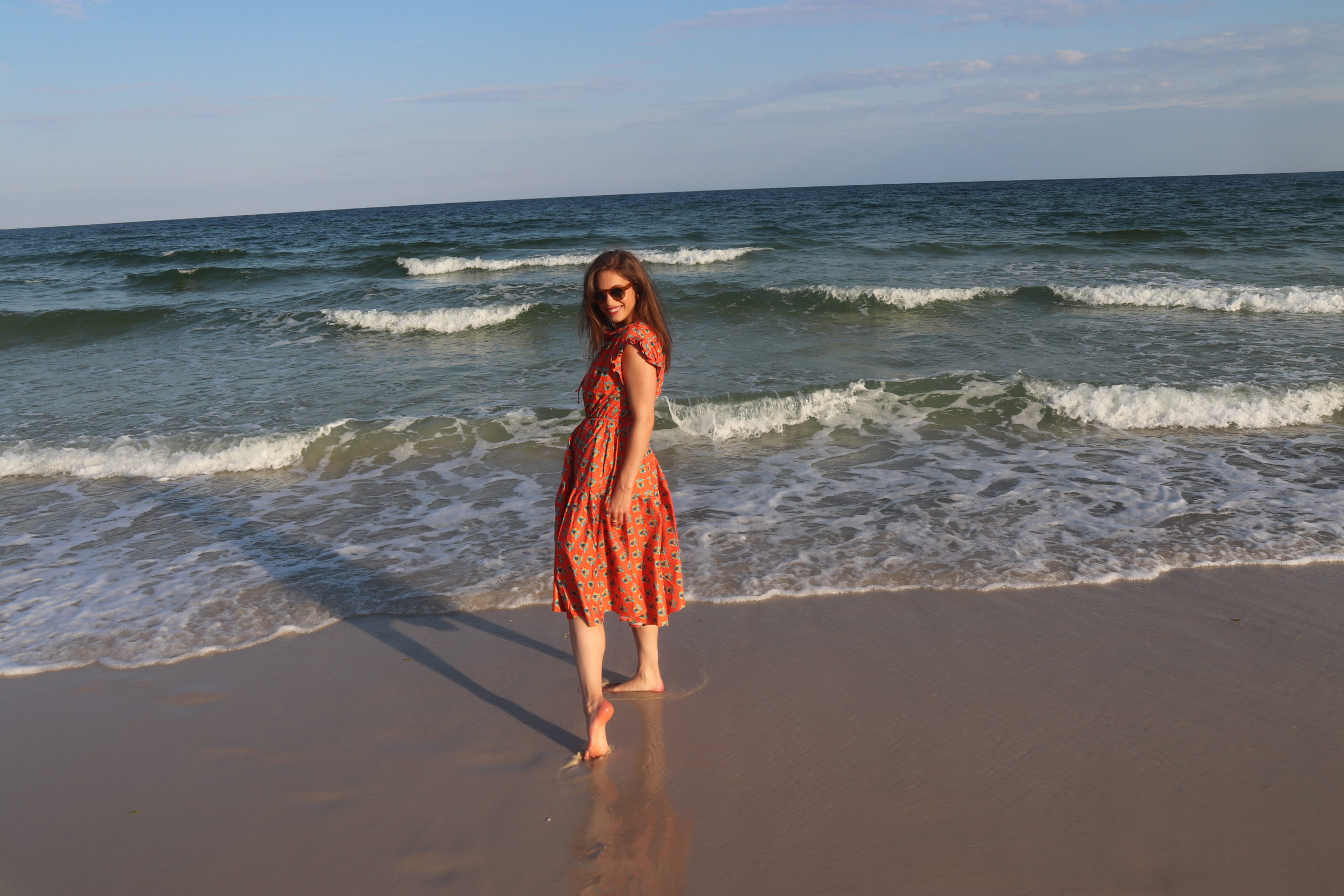 Girl in an orange dress with brown hair on the beach barefoot