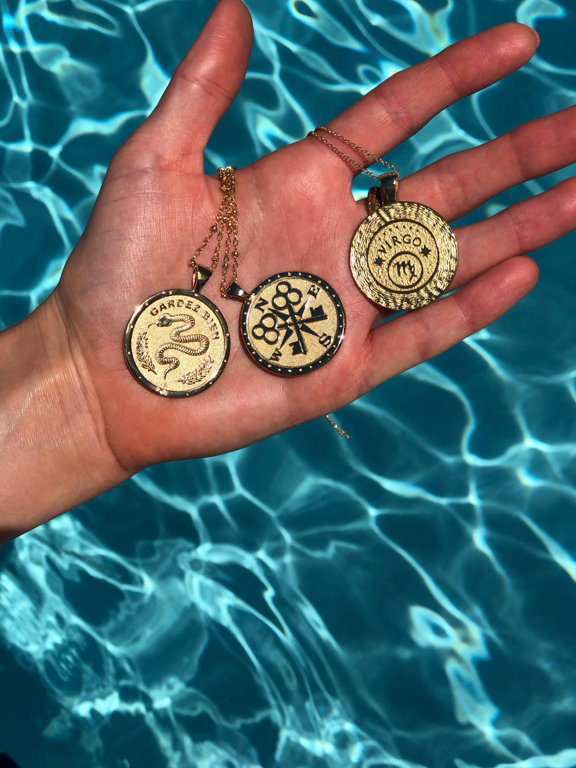 hand holding three gold pendants over a pool