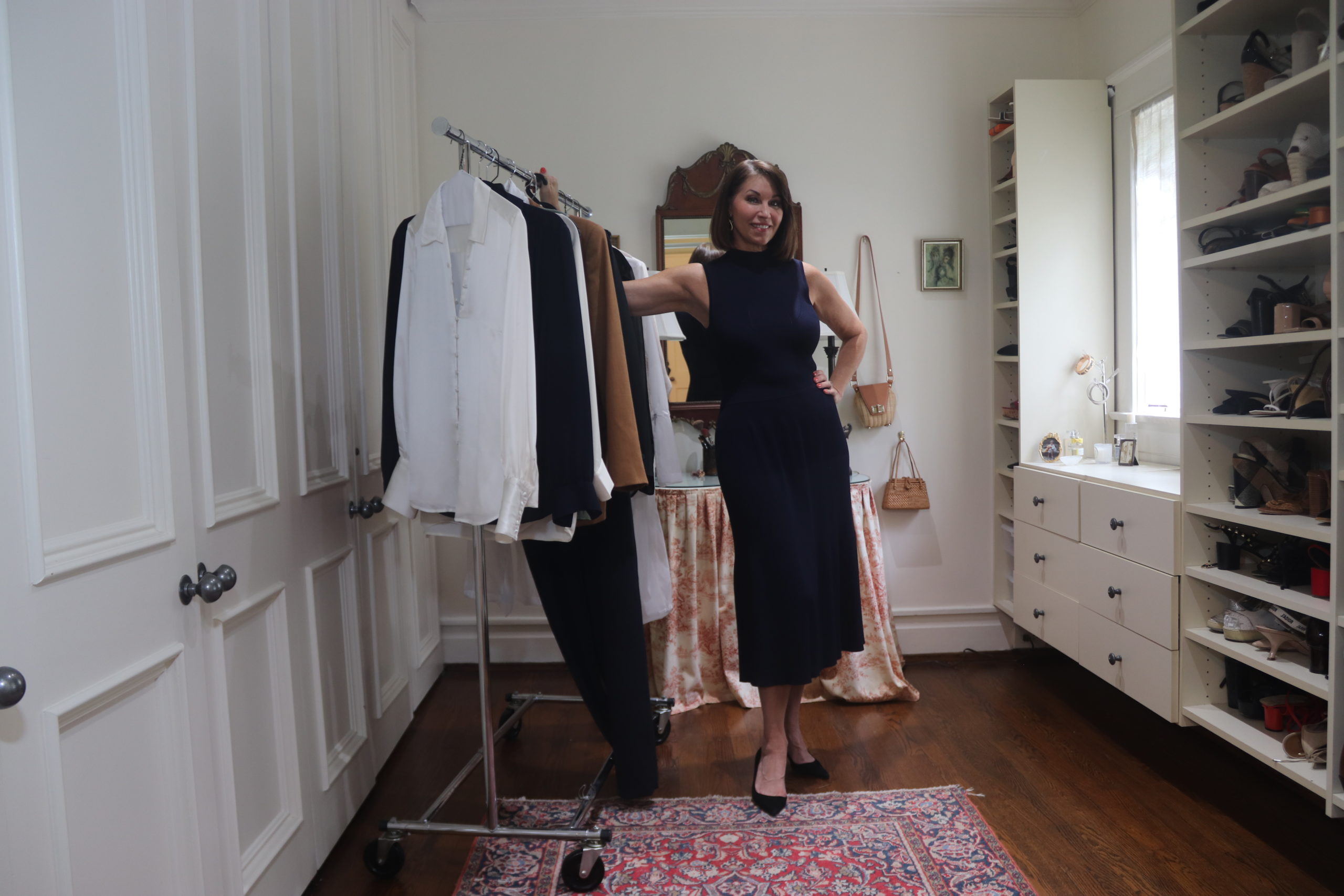 A woman standing in a closet wearing a navy sleeveless dress wearing manolo blank pumps. She has brown hair