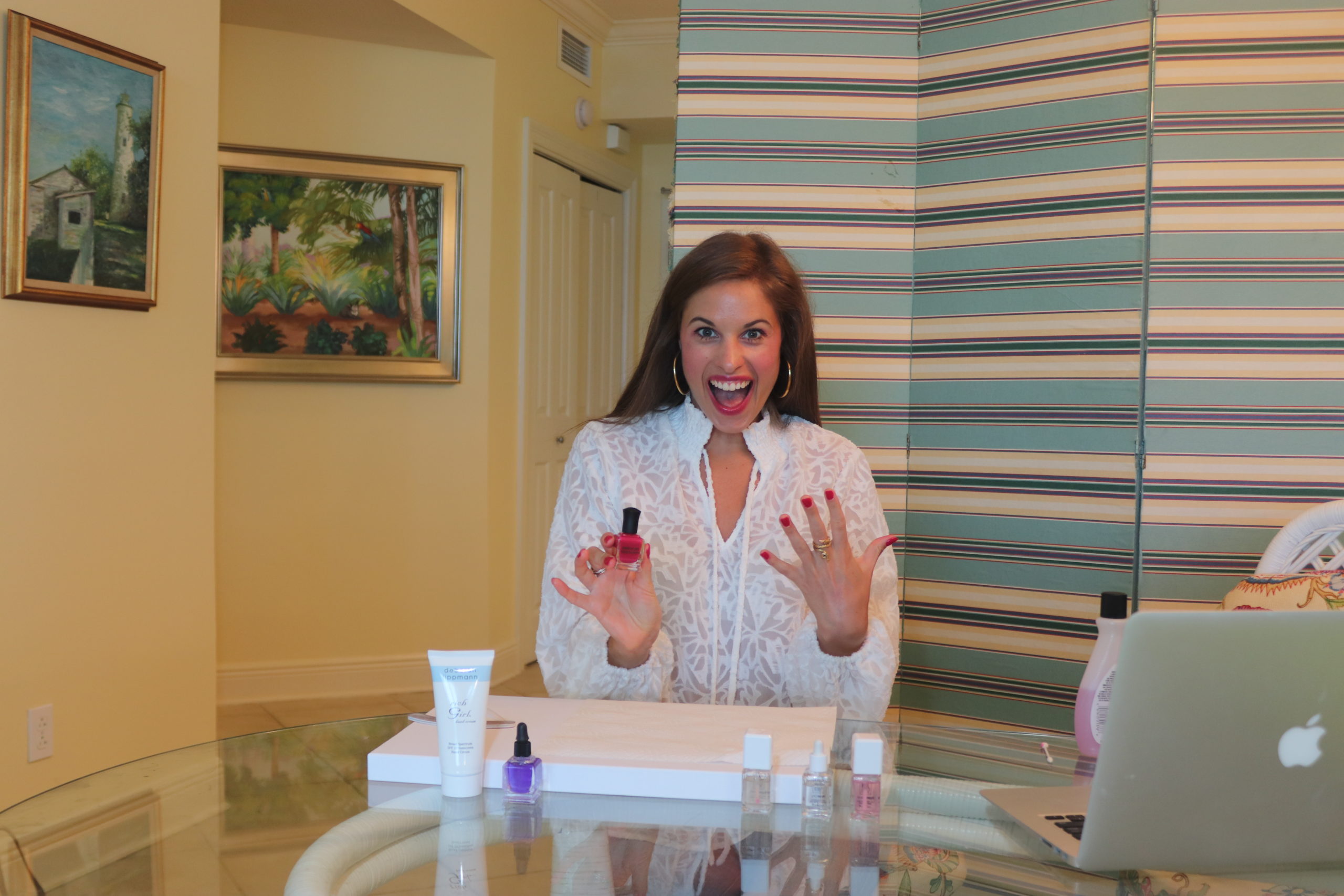 Woman sitting at a table with manicure supplies. She has brown hair and is wearing a white shirt