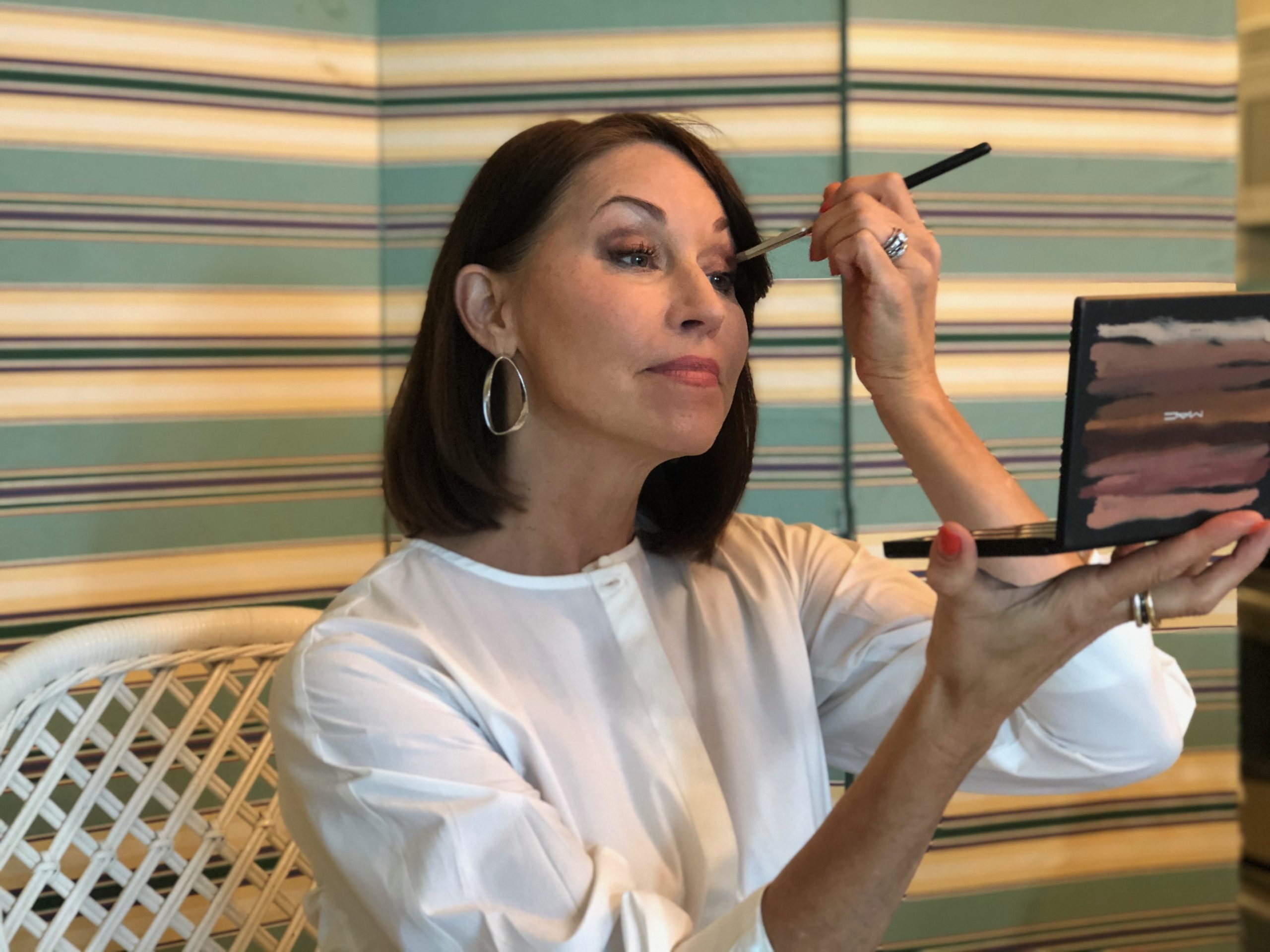 Woman with brown hair wearing a white shirt putting on makeup
