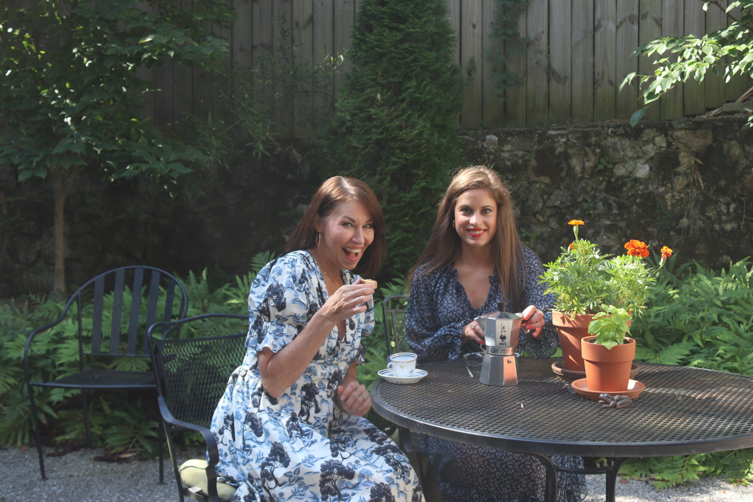 Two women sitting in a backyard drinking espresso & eating biscotti