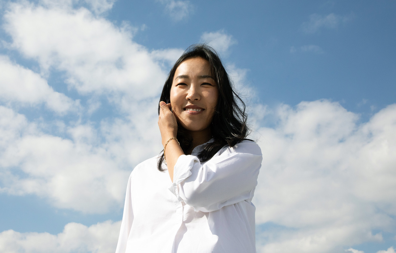 Asian woman wearing a white button down shirt with a blue sky with white clouds in the background