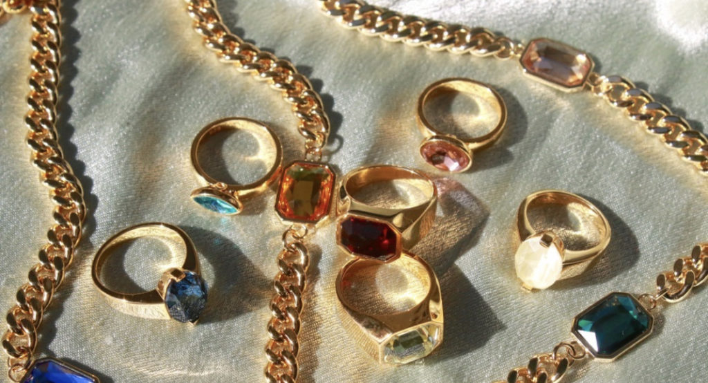 Gold costume jewelry with bright jewel-tone stones on a green background