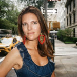 White woman with brown hair in NYC looking at camera wearing gold statement earrings with red fringe