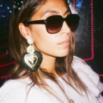 Brown skinned woman wearing sunglasses & gold & black heart statement earrings