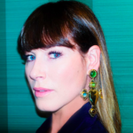 White woman with brown hair & bands wearing multi-colored cross statement earrings