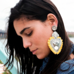 Brown skinned woman wearing silver & yellow fringe heart statement earrings