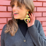 White woman with brown hair wearing gold heart statement earrings with pearls