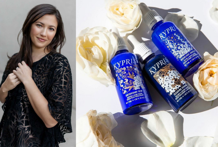 Asian woman smiling & looking at the camera wearing a black top and 3 blue drop bottle beauty products