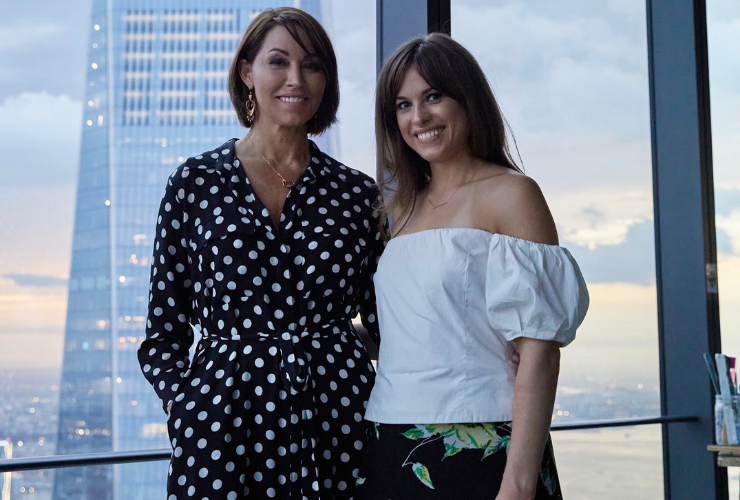 Two brown haired women smiling and looking at the camera in front of One World Trade