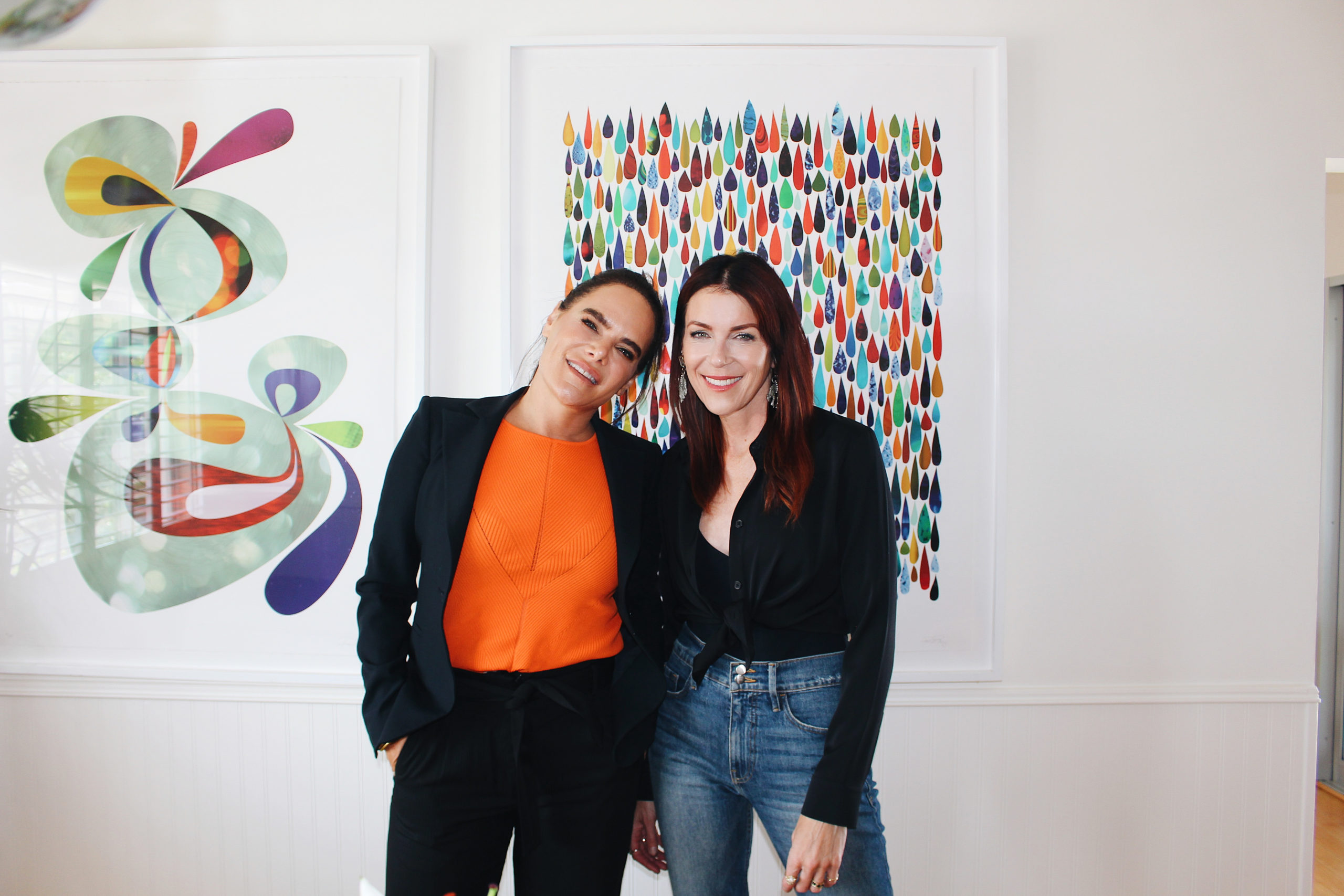 Two white women with brown hair smile at the camera in front of colorful art