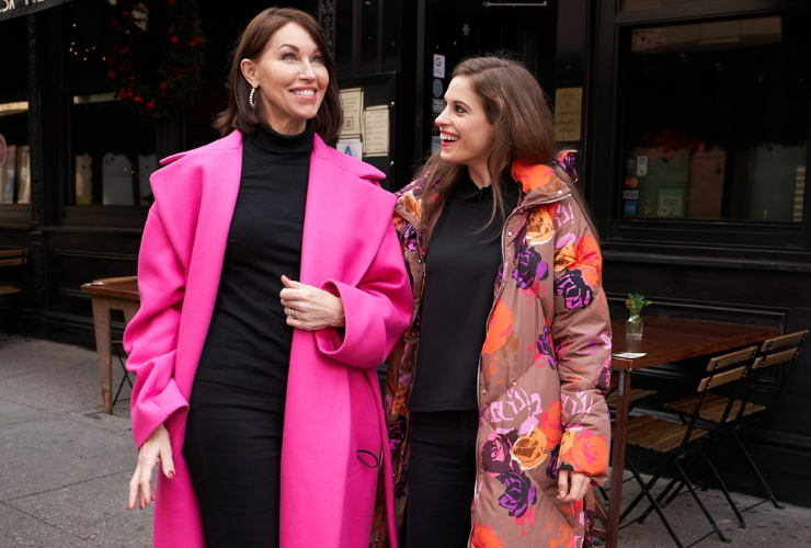 Two white women with brown hair smiling wearing pink coats