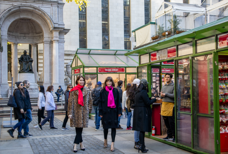 Two women with brown hair walking through a holiday market smiling