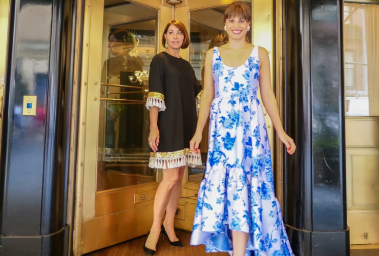 Two women with brown hair smiling & looking at the camera in cocktail dresses