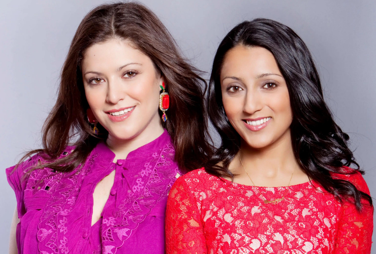 Two women looking at the camera & smiling; they wear pink & red lace tops