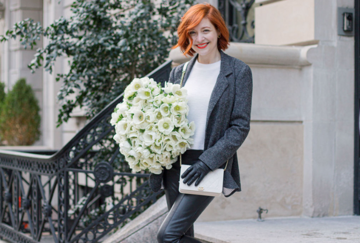 White woman with red hair carrying a bouquet of flowers on the stairs & smiling