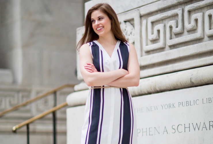 White girl with brown hair wearing a navy & white striped sleeveless dress standing in front of the New York Public Library
