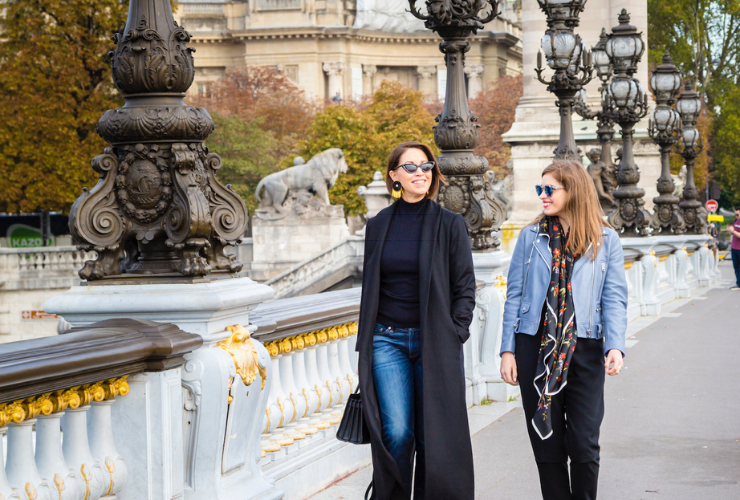 Two white women with brown hair walking on a bridge in Paris