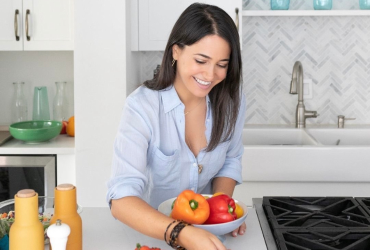 White woman with brown hair holding bell peppers smiling in a kitchen
