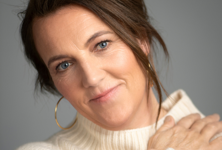 white woman with brown hair wearing a cream sweater close up of her face smiling and looking at the camera