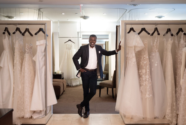 black man in a suit standing in front of racks of wedding gowns
