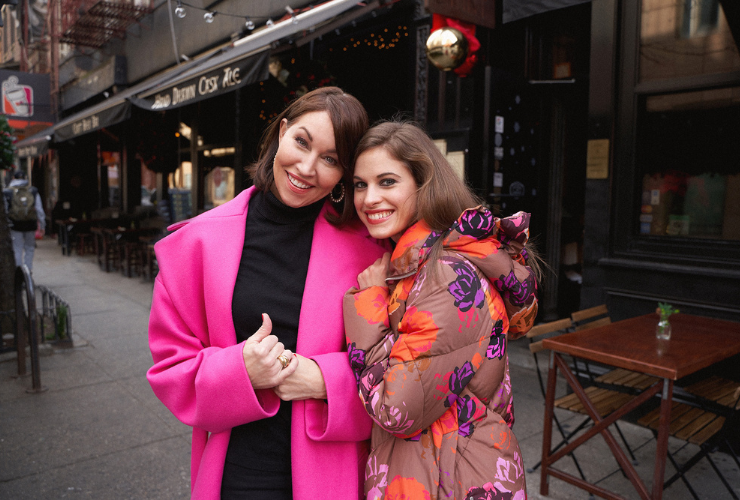 two white women with brown hair wear pink coats & smile at the camera