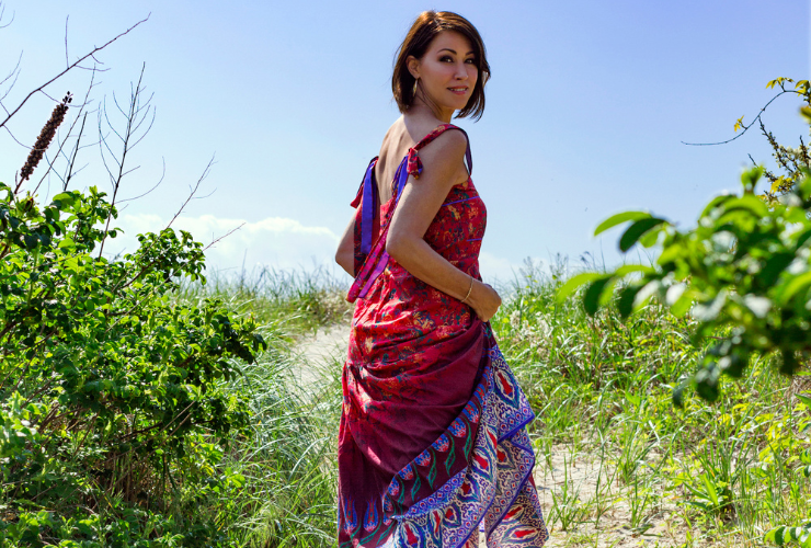 white woman with brown hair walking on the beach wearing a red printed sleeveless dress