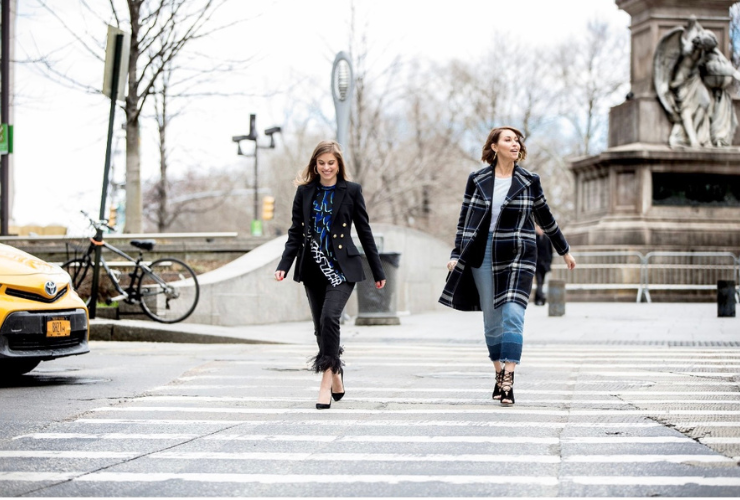 Two white women with brown hair walk across a crosswalk in NYC