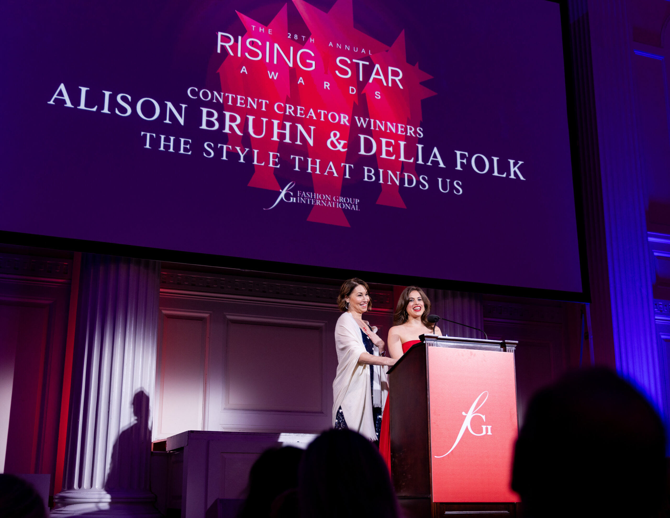 Two women receive their award and are recognized on stage at a fashion event in New York City.
